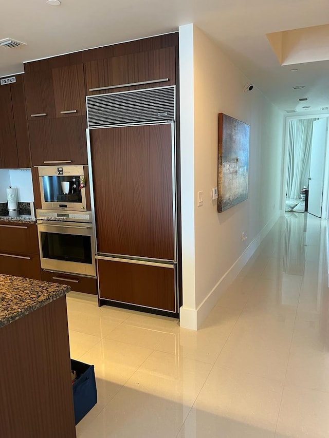 15811 Collins Ave Unit 1502, Sunny Isles Beach, FL 33160 - kitchen featuring paneled fridge, modern cabinets, dark brown cabinetry, dark stone counters, and light tile patterned floors
