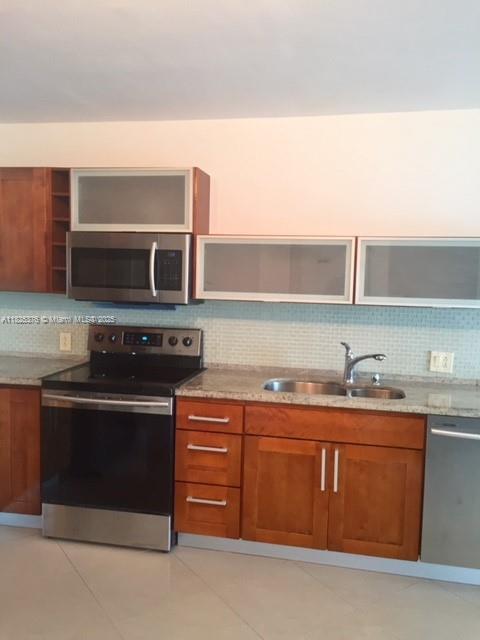 3375 N Country Club Dr Unit 1508, Aventura, FL 33180 - kitchen featuring appliances with stainless steel finishes, open shelves, brown cabinetry, backsplash, and light tile patterned flooring