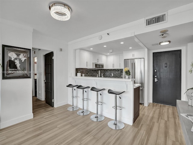 1470 NE 123rd St Unit Aph9, North Miami, FL 33161 - kitchen with stainless steel appliances, light wood-style floors, white cabinetry, a peninsula, and decorative backsplash