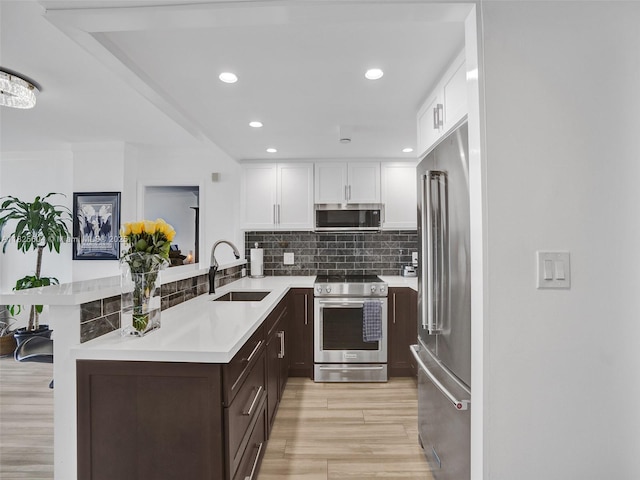 1470 NE 123rd St Unit Aph9, North Miami, FL 33161 - kitchen with appliances with stainless steel finishes, dark brown cabinetry, light countertops, white cabinets, and light wood-type flooring