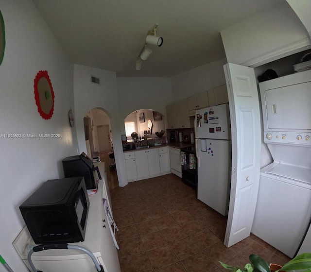 985 NE 34th Ave Unit 203, Homestead, FL 33033 - kitchen featuring stacked washing machine and dryer, freestanding refrigerator, dark countertops, dark tile patterned flooring, and arched walkways