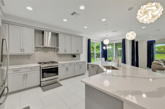 13307 SW Green Delta Rd, Port St Lucie, FL 34987 - kitchen with stainless steel gas range oven, wall chimney range hood, backsplash, light tile patterned floors, and hanging light fixtures