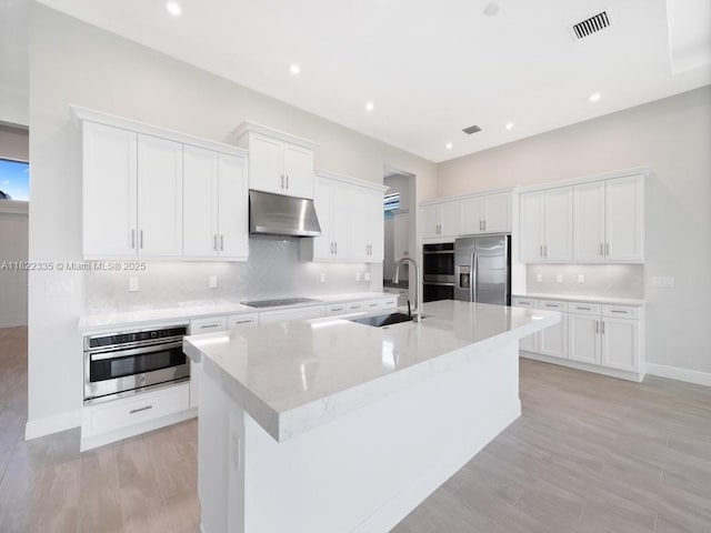 9125 SW Esule Way, Port St Lucie, FL 34987 - kitchen featuring under cabinet range hood, stainless steel appliances, an island with sink, backsplash, and white cabinets