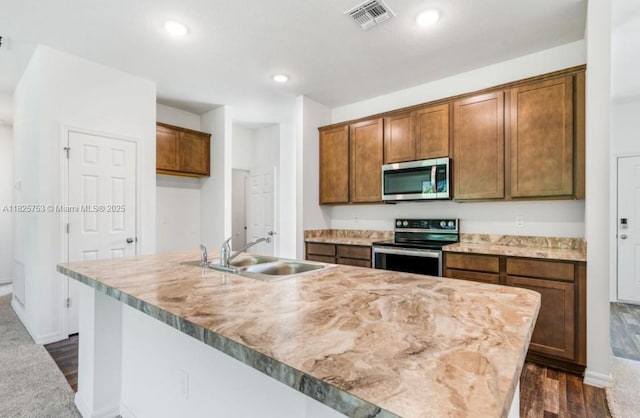 485 SW Molloy St, Port St Lucie, FL 34984 - kitchen with stainless steel appliances, a center island with sink, dark wood-type flooring, recessed lighting, and brown cabinetry
