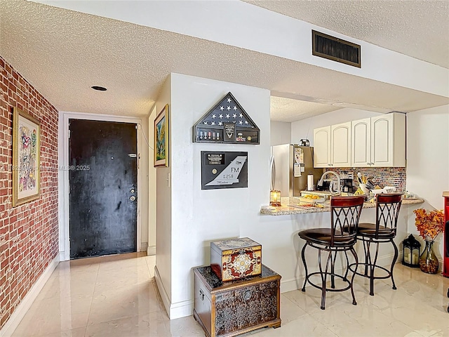 8635 NW 8th St Unit 103, Miami, FL 33126 - kitchen with freestanding refrigerator, a textured ceiling, brick wall, a kitchen bar, and backsplash