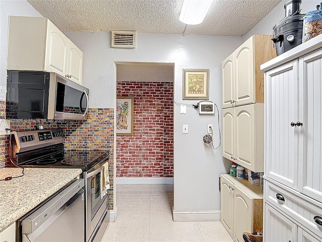 8635 NW 8th St Unit 103, Miami, FL 33126 - kitchen featuring stainless steel appliances, a textured ceiling, light tile patterned flooring, brick wall, and decorative backsplash