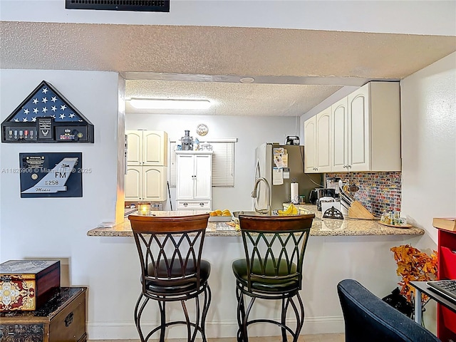 8635 NW 8th St Unit 103, Miami, FL 33126 - kitchen with freestanding refrigerator, a peninsula, white cabinets, a kitchen bar, and backsplash