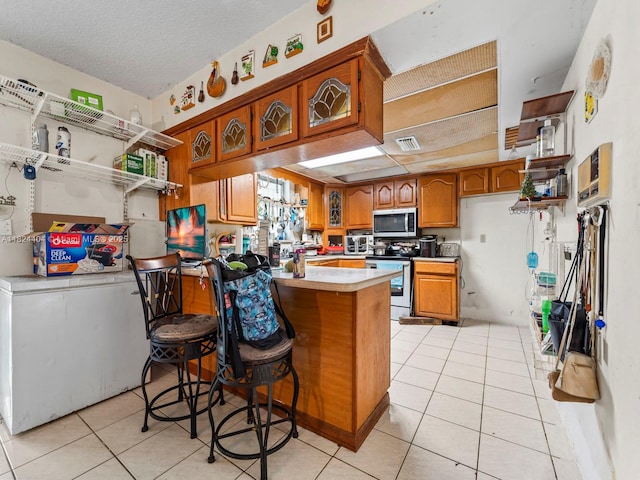 17430 SW 92nd Ct, Palmetto Bay, FL 33157 - kitchen featuring stainless steel appliances, brown cabinets, light tile patterned floors, a peninsula, and a textured ceiling