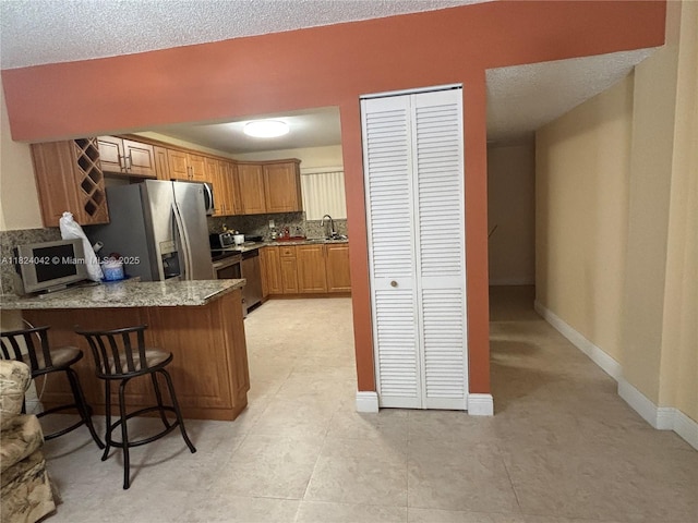 1635 W 44th Pl Unit 509, Hialeah, FL 33012 - kitchen with stainless steel fridge, a peninsula, a breakfast bar, brown cabinetry, and light stone countertops