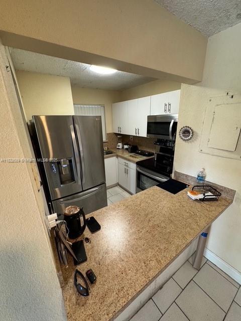 8841 W Flagler St Unit 108, Miami, FL 33174 - kitchen with stainless steel appliances, a textured ceiling, light tile patterned floors, white cabinets, and a peninsula