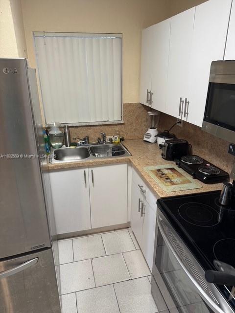 8841 W Flagler St Unit 108, Miami, FL 33174 - kitchen with stainless steel appliances, white cabinets, light countertops, and light tile patterned flooring