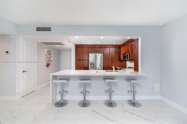 5555 Collins Ave Unit 7N, Miami Beach, FL 33140 - kitchen with stainless steel appliances, a peninsula, light countertops, light marble finish floors, and a breakfast bar