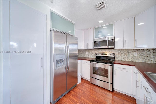 6440 NW 114th Ave Unit 434, Doral, FL 33178 - kitchen featuring appliances with stainless steel finishes, dark countertops, light wood-style flooring, a textured ceiling, and glass insert cabinets