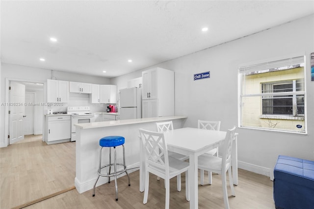 1408 N 23rd St, Fort Pierce, FL 34950 - kitchen with white appliances, light wood finished floors, white cabinets, a breakfast bar area, and light countertops
