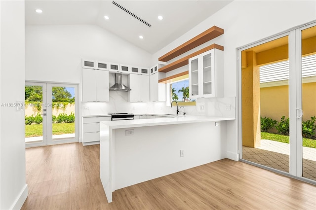 9047 Baybury Ln, West Palm Beach, FL 33411 - kitchen with wall chimney exhaust hood, light countertops, a peninsula, light wood-type flooring, and white cabinetry