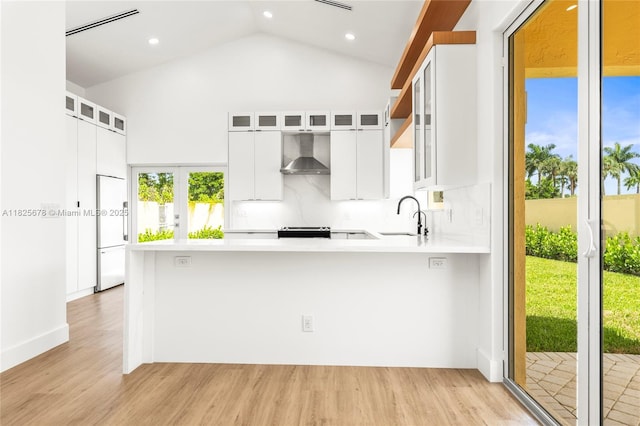 9047 Baybury Ln, West Palm Beach, FL 33411 - kitchen with wall chimney exhaust hood, light countertops, high end white refrigerator, light wood-type flooring, and a peninsula