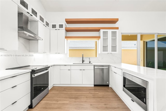 9047 Baybury Ln, West Palm Beach, FL 33411 - kitchen featuring appliances with stainless steel finishes, wall chimney range hood, decorative backsplash, light wood-style floors, and light countertops