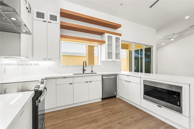 9047 Baybury Ln, West Palm Beach, FL 33411 - kitchen featuring appliances with stainless steel finishes, ventilation hood, backsplash, light wood-style flooring, and white cabinets