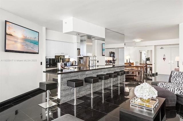 4779 Collins Ave Unit 702, Miami Beach, FL 33140 - kitchen with a kitchen bar, dark countertops, white cabinetry, and dark tile patterned floors