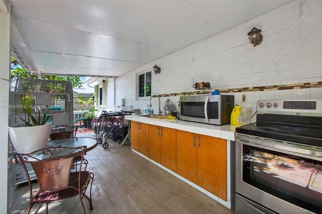 8905 NW 112th St, Hialeah Gardens, FL 33018 - kitchen featuring stainless steel appliances, wood finished floors, tile countertops, a textured wall, and brown cabinetry