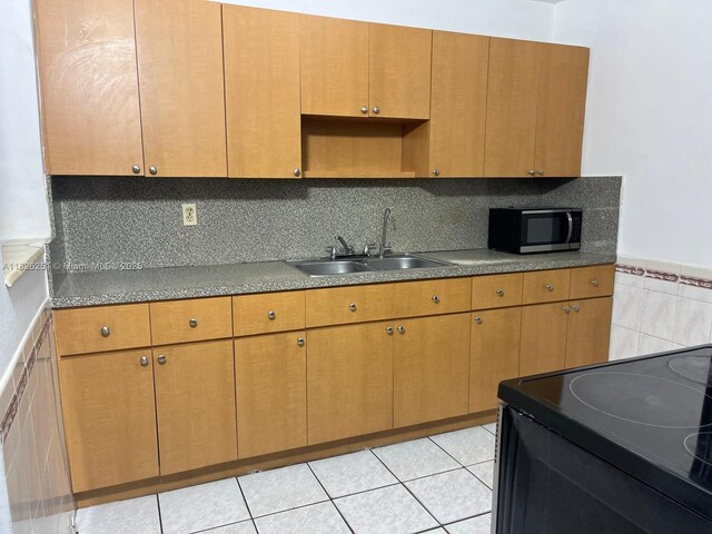 217 E 20th St, Hialeah, FL 33010 - kitchen featuring black electric range oven, light tile patterned floors, wainscoting, tile walls, and brown cabinets