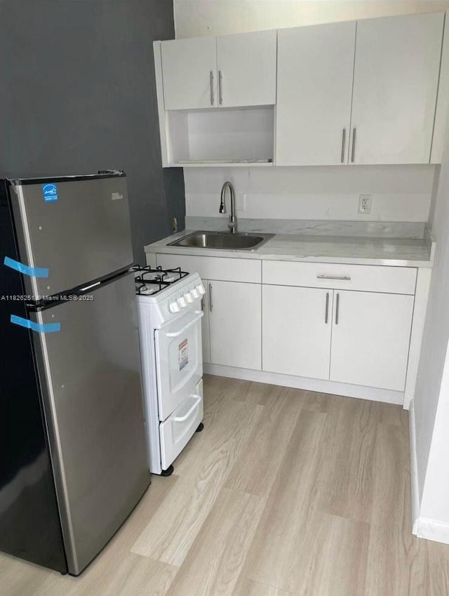 217 E 20th St, Hialeah, FL 33010 - kitchen featuring freestanding refrigerator, white range with gas cooktop, light wood-style floors, light countertops, and white cabinets
