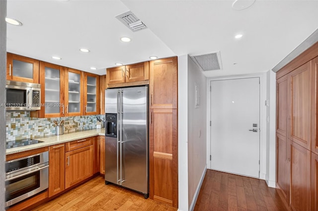 2555 Collins Ave Unit 606, Miami Beach, FL 33140 - kitchen with appliances with stainless steel finishes, light wood-style floors, brown cabinets, light stone countertops, and glass insert cabinets