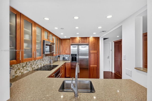 2555 Collins Ave Unit 606, Miami Beach, FL 33140 - kitchen featuring appliances with stainless steel finishes, recessed lighting, light stone counters, backsplash, and glass insert cabinets