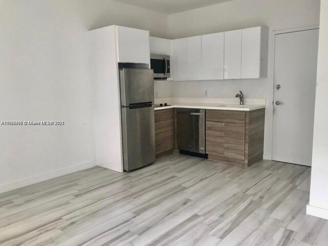 1560 Meridian Ave Unit 206, Miami Beach, FL 33139 - kitchen featuring appliances with stainless steel finishes, light countertops, white cabinets, and light wood-style flooring
