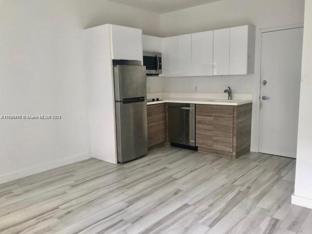 1560 Meridian Ave Unit 206, Miami Beach, FL 33139 - kitchen featuring appliances with stainless steel finishes, light countertops, white cabinetry, and light wood-style flooring