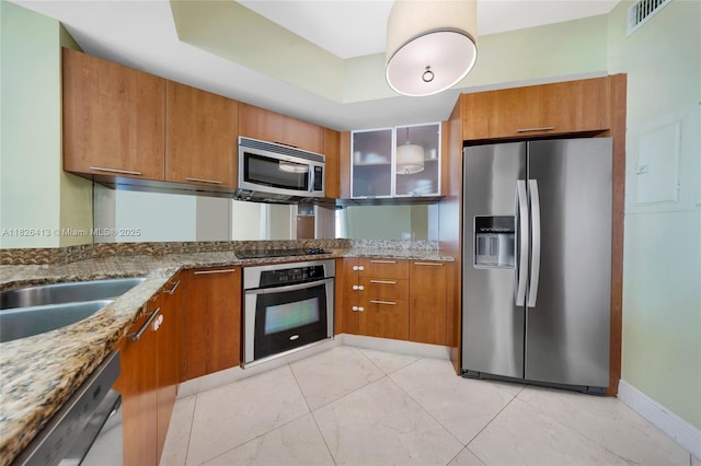 480 NE 30th St Unit 1402, Miami, FL 33137 - kitchen featuring stainless steel appliances, brown cabinetry, light stone countertops, glass insert cabinets, and light tile patterned flooring