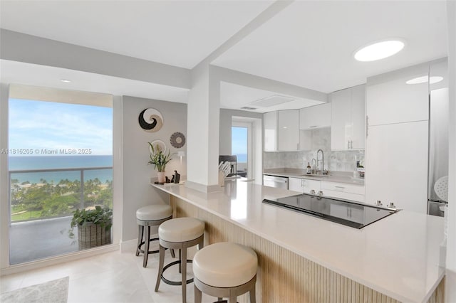 2701 N Ocean Blvd Unit 18A, Fort Lauderdale, FL 33308 - kitchen featuring a kitchen bar, light countertops, white cabinetry, black electric stovetop, and light tile patterned floors