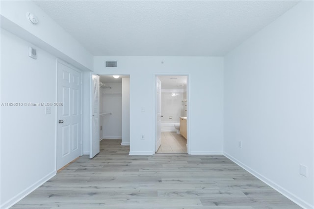 1919 Van Buren St Unit 205A, Hollywood, FL 33020 - unfurnished bedroom with light wood-type flooring, a closet, a textured ceiling, ensuite bath, and a walk in closet