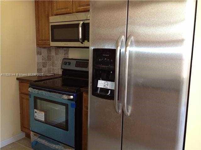 8917 NW 28th Dr Unit C-51, Coral Springs, FL 33065 - kitchen with appliances with stainless steel finishes, backsplash, brown cabinets, dark countertops, and light tile patterned floors