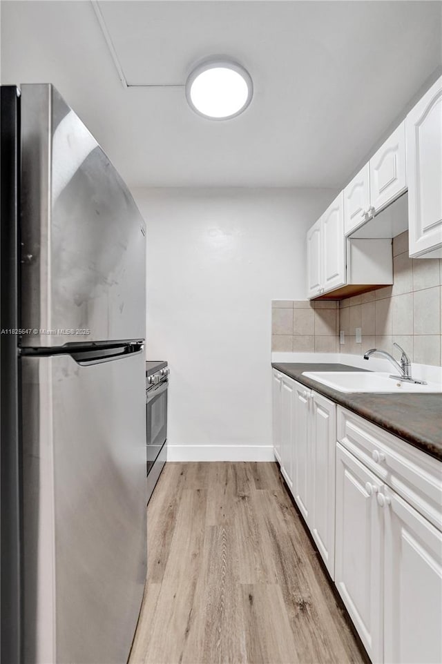 2106 NE 56th Ct Unit 108, Fort Lauderdale, FL 33308 - kitchen with appliances with stainless steel finishes, light wood finished floors, white cabinetry, dark countertops, and decorative backsplash