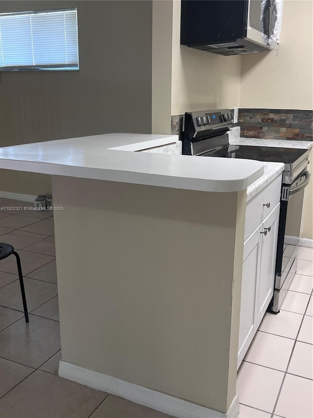 15 Crossings Cir Unit F, Boynton Beach, FL 33435 - kitchen with stainless steel range with electric stovetop, light tile patterned floors, white cabinets, light countertops, and a peninsula