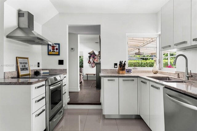600 NE 55th Ter, Miami, FL 33137 - kitchen with stainless steel appliances, wall chimney range hood, light stone counters, white cabinets, and light tile patterned floors