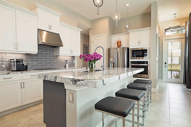 9190 SW Esule Way, Port St Lucie, FL 34987 - kitchen with stainless steel appliances, under cabinet range hood, decorative backsplash, a breakfast bar area, and a kitchen island with sink