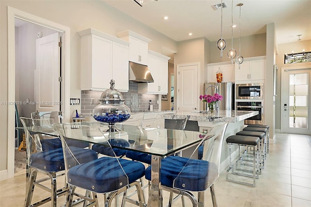 9190 SW Esule Way, Port St Lucie, FL 34987 - kitchen with stainless steel appliances, under cabinet range hood, decorative backsplash, a center island with sink, and white cabinetry