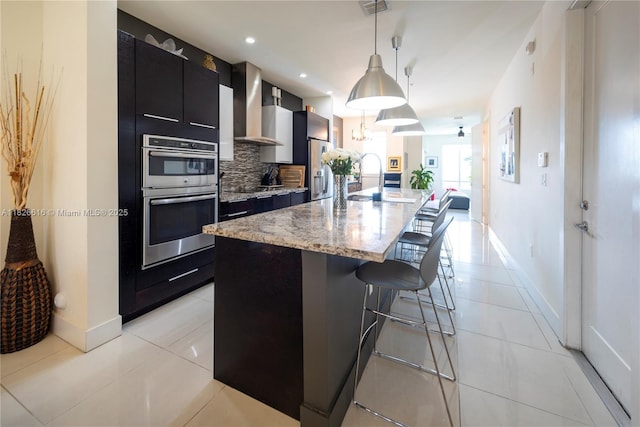 10260 NW 63rd Ter Unit 208, Doral, FL 33178 - kitchen with appliances with stainless steel finishes, wall chimney range hood, dark cabinetry, a breakfast bar area, and light tile patterned floors