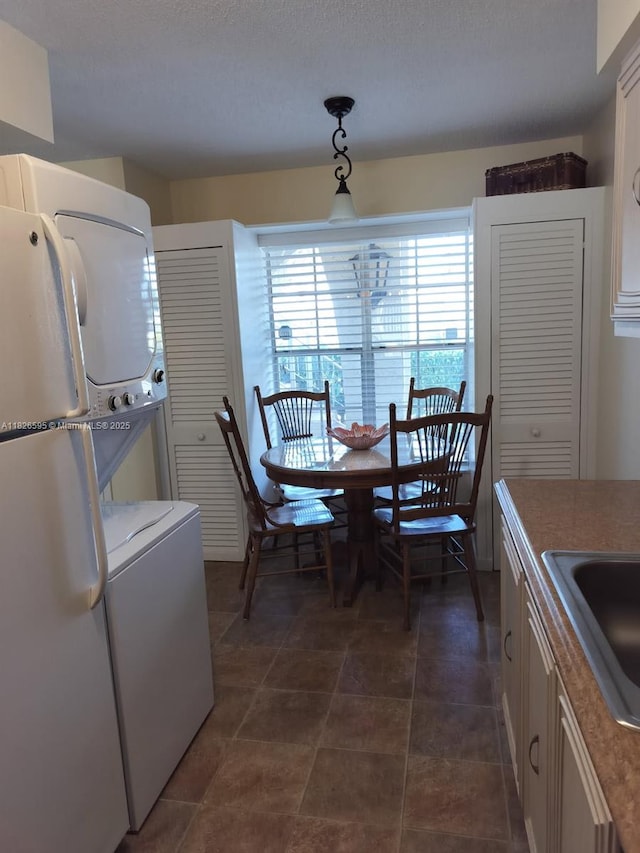 13791 Flora Pl Unit B, Delray Beach, FL 33484 - kitchen featuring stacked washer / dryer, freestanding refrigerator, pendant lighting, a textured ceiling, and white cabinets