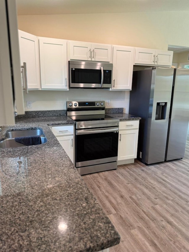 5029 N Dogwood Cir, La Belle, FL 33935 - kitchen featuring stainless steel appliances, white cabinetry, light wood-style floors, dark stone counters, and vaulted ceiling