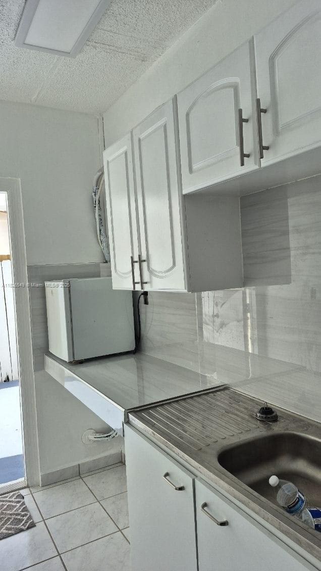 7322 SW 134th Pl, Miami, FL 33183 - kitchen with white cabinets, light tile patterned floors, fridge, and a textured ceiling