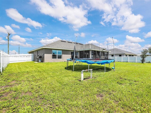 2405 Nelson Rd, Cape Coral, FL 33993 - back of house featuring a trampoline, stucco siding, and a fenced backyard