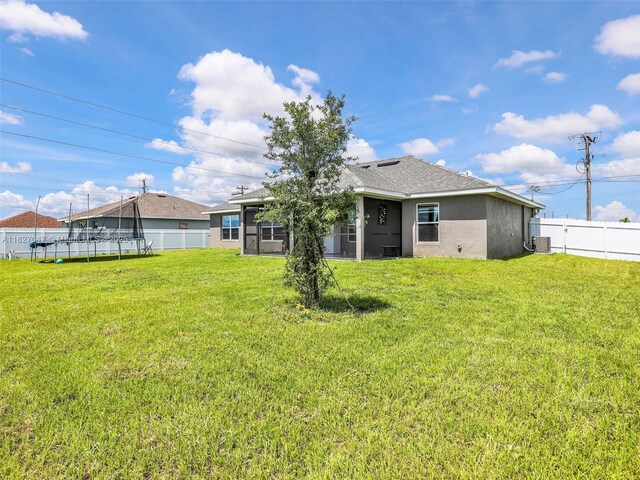 2405 Nelson Rd, Cape Coral, FL 33993 - rear view of property featuring a trampoline, a fenced backyard, stucco siding, and roof with shingles