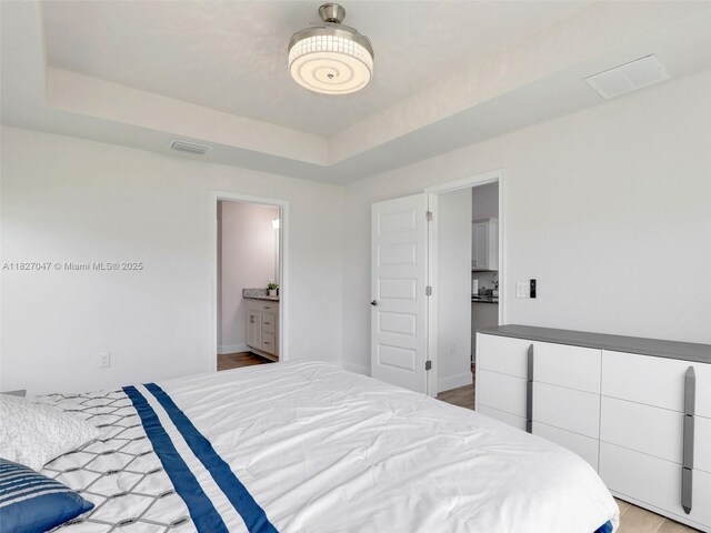 2405 Nelson Rd, Cape Coral, FL 33993 - bedroom with a tray ceiling, wood finished floors, and connected bathroom
