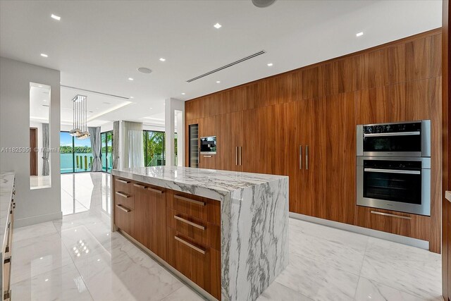 1311 Stillwater Dr, Miami Beach, FL 33141 - kitchen featuring modern cabinets, brown cabinets, double oven, a spacious island, and light stone counters