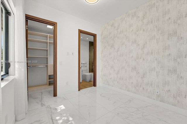 1311 Stillwater Dr, Miami Beach, FL 33141 - unfurnished bedroom featuring wallpapered walls, a spacious closet, marble finish flooring, a closet, and an accent wall