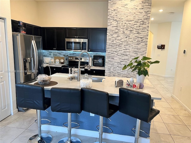 134 NE 23rd Ter, Homestead, FL 33033 - kitchen featuring stainless steel appliances, dark cabinetry, decorative backsplash, light countertops, and a kitchen bar