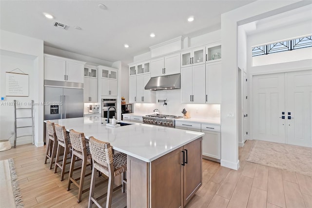 20161 SE Bridgewater Dr, Jupiter, FL 33458 - kitchen featuring under cabinet range hood, appliances with stainless steel finishes, light wood-style floors, a large island with sink, and white cabinets